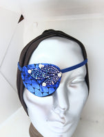 Women's high-fashion eye patch "MIDNIGHT MADNESS" is expertly handmade with blue metallic fabric overlaid with sequin fabric and adorned with 4 pearls. A matching elastic band and a soft backing of recycled fabric provide comfort. An exciting design that