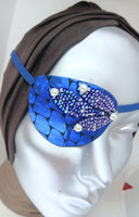Women's high-fashion eye patch "MIDNIGHT MADNESS" is expertly handmade with blue metallic fabric overlaid with sequin fabric and adorned with 4 pearls. A matching elastic band and a soft backing of recycled fabric provide comfort. An exciting design that