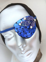 Women's high-fashion eye patch "MIDNIGHT MADNESS" is expertly handmade with blue metallic fabric overlaid with sequin fabric and adorned with 4 pearls. A matching elastic band and a soft backing of recycled fabric provide comfort. An exciting design that