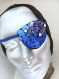 Women's high-fashion eye patch "MIDNIGHT MADNESS" is expertly handmade with blue metallic fabric overlaid with sequin fabric and adorned with 4 pearls. A matching elastic band and a soft backing of recycled fabric provide comfort. An exciting design that